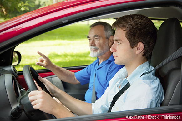 A photo of a teenage boy driving a car with father giving instructions